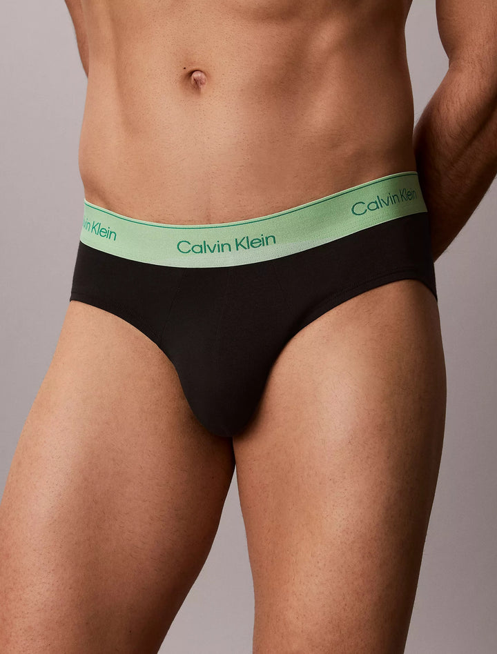 Close-up front view of Calvin Klein Pride brief waistband in mint green on black, grey studio background